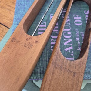 May include: Two wooden weaving shuttles with smooth, elongated bodies and central cutouts. The left shuttle is stamped with the word DRYAD. They are positioned over a book cover featuring the text THE LANGUAGE OF and Jean-Michel.