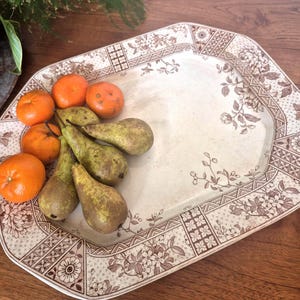 May include: A rectangular, cream-coloured serving platter with a brown floral and geometric border. The platter holds several green pears and orange tangerines. The vintage-style design is suitable for serving fruit, on a wooden surface.