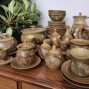 May include: A collection of brown and tan pottery with a swirling pattern. The pottery includes bowls, plates, cups, a teapot, and a sugar bowl.