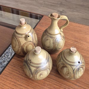 May include: Set of four brown and tan ceramic salt and pepper shakers and a jug with cork stoppers. The shakers and jug have a swirling pattern.