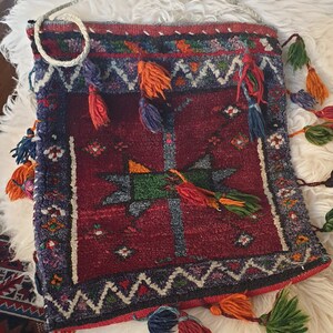 May include: A red, blue, and green woven bag with tassels. The bag has a geometric pattern and is made of a thick, textured fabric.