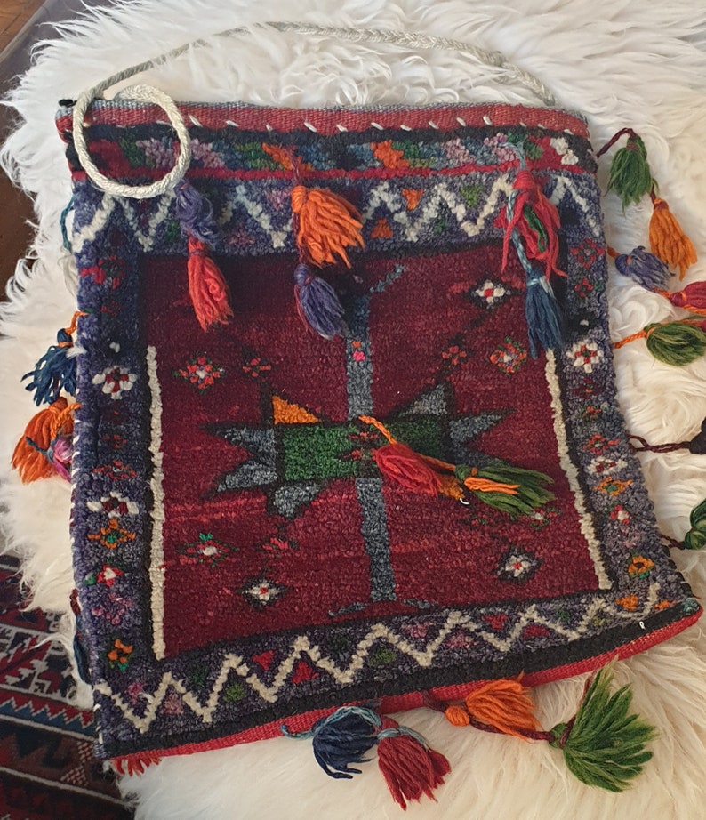 May include: A red, blue, and green woven bag with tassels. The bag has a geometric pattern and is made of a thick, textured fabric.