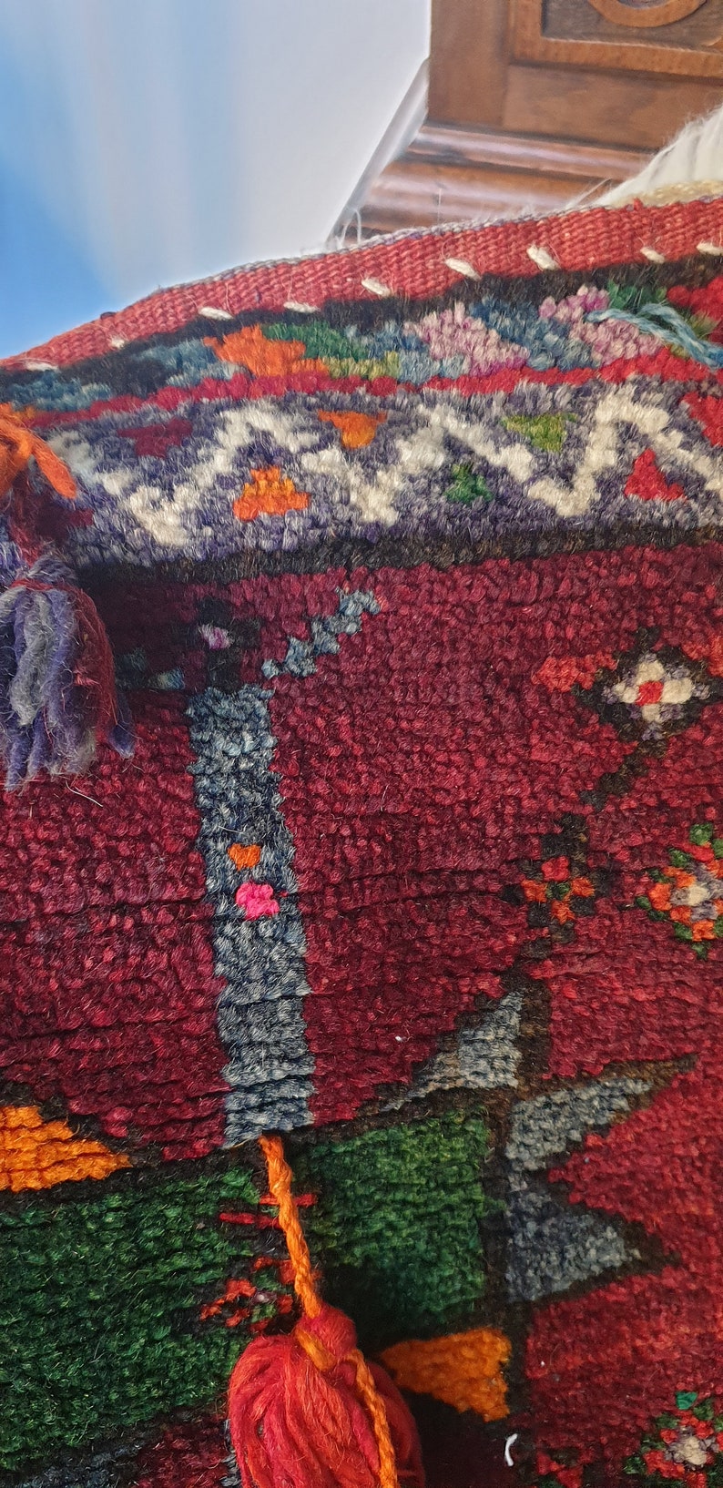 May include: A close-up of a colorful woven rug with tassels. The rug has a red, green, blue, and orange pattern. The tassels are red and orange.