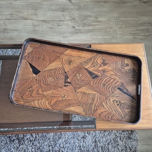May include: A rectangular wooden serving tray featuring a complex geometric marquetry pattern made of various wood grains in shades of brown. The surface is decorated with small, inlaid symbols within the triangular and quadrilateral segments.