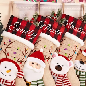 Könnte beinhalten: Weihnachtsstrümpfe mit Namen in weißer Schrift auf einer rot-schwarz karierten Manschette. Jeder Strumpf hat einen Körper aus Jute mit festlichen Designs und Gesichtern von Figuren.