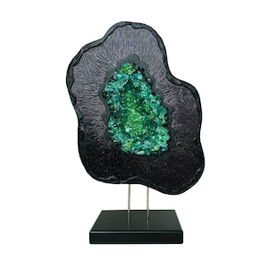 May include: A black and green glass sculpture with a textured surface and a green crystal-like center. The sculpture is on a black stand.