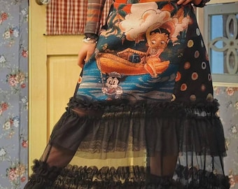 Könnte beinhalten: Ein langer, gestufter Rock mit einem Cartoon-Aufdruck von Betty Boop in einem Boot mit Micky Maus. Der Rock hat einen schwarzen Tüll-Overlay mit Rüschen. Das Model trägt ein kariertes Langarmshirt.