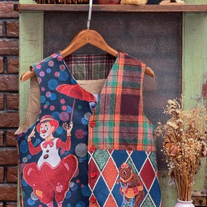 May include: A multi-coloured patchwork waistcoat with a clown and a bear riding a bicycle on the front. The waistcoat has a plaid pattern, a diamond pattern, and a pattern of colourful circles.