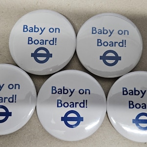 May include: Five white circular badges, each displaying the text "Baby on Board!" in blue, accompanied by a blue circular design. The badges are arranged on a light surface.