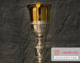May include: A silver chalice with a gold-toned bowl and a decorative base. The chalice is a religious artifact used in Catholic ceremonies.