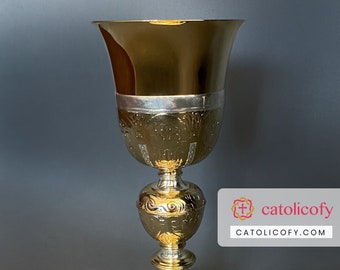 May include: A gold chalice with intricate engraved designs. The chalice has a wide, flared base and a tall, slender stem. The chalice is a religious artifact used in Catholic ceremonies.