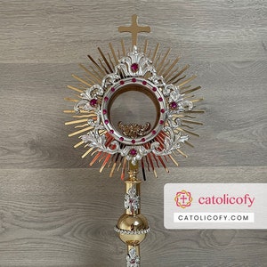 May include: A gold-plated monstrance with a silver-plated inner circle and red jewels. The monstrance is on a gold-plated stand with a round base.