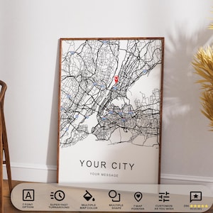 May include: A framed map print featuring a detailed black and white city map with a red marker. The text "YOUR CITY" and "YOUR MESSAGE" are at the bottom. The print is displayed near a wooden chair and decorative plant.