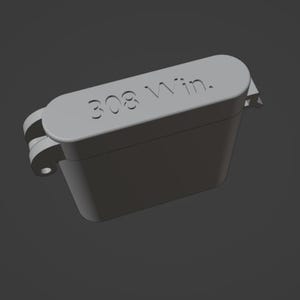 Puede incluir: Un contenedor rectangular gris con tapa abisagrada. El texto "308 Win." está grabado en la tapa. El contenedor tiene una parte superior redondeada y un pequeño pestillo lateral.