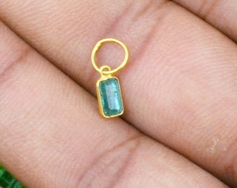 Puede incluir: Un charm de oro con una piedra preciosa de esmeralda verde. El charm es de forma rectangular y tiene un pequeño bucle en la parte superior para sujetarlo a un collar o pulsera.
