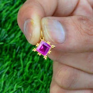 Può includere: Un ciondolo d'oro con una pietra preziosa rosa quadrata circondata da piccole perle dorate.