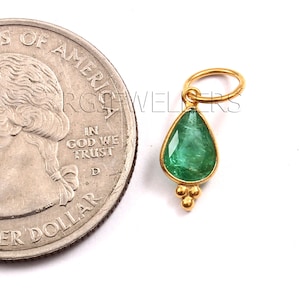 May include: A gold pendant with a pear-shaped emerald gemstone. The pendant has a small loop at the top for attaching to a chain.