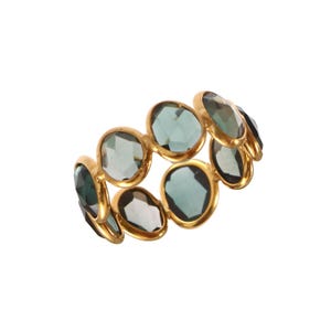 May include: A gold-colored ring featuring multiple oval-shaped, teal-colored gemstones. The gemstones are set closely together, creating a continuous band of color. The ring is set against a white background.