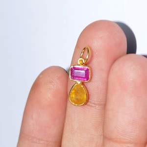 May include: A gold pendant featuring a pink rectangular gemstone and a yellow teardrop-shaped gemstone.