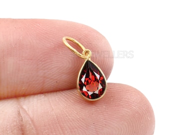 Puede incluir: Un colgante de oro con una piedra preciosa roja en forma de lágrima.