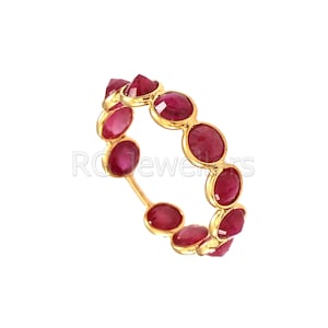 Peut inclure: Une bague en or avec une bande de pierres précieuses rouges. Les pierres précieuses sont rondes et ont un sommet légèrement pointu.