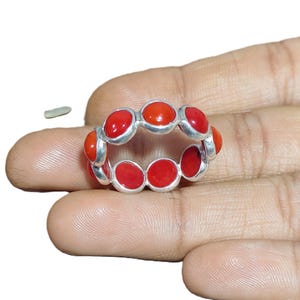 May include: A silver ring featuring a series of vibrant red coral stones. The ring's design showcases a continuous band of oval-shaped coral gems, set in a polished silver band. The coral stones are a bright, eye-catching red.