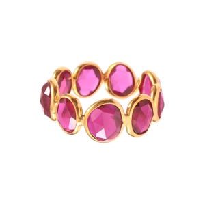 May include: A gold-toned ring featuring a series of vibrant, faceted, oval-shaped pink gemstones. The gemstones are set closely together, creating a continuous band of color. The ring's design is simple yet elegant, with a focus on the gemstones' brilliance.