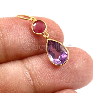May include: Gold dangle earrings with a teardrop shaped amethyst gemstone and a round ruby gemstone.