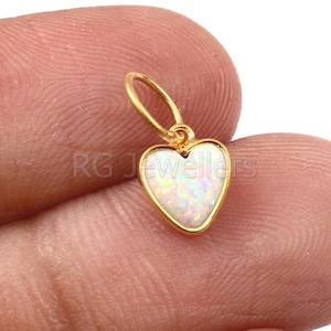 May include: A gold heart-shaped pendant with a white opal stone. The pendant has a small loop at the top for attaching to a chain.
