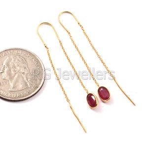 May include: A pair of gold chain earrings with red oval gemstones. The earrings are about the size of a US quarter.