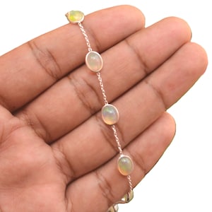 May include: A delicate silver chain bracelet featuring four evenly spaced, oval-shaped cabochon opals. Each opal is set in a simple silver bezel, showcasing a milky white appearance with subtle iridescent flashes of color along the chain.