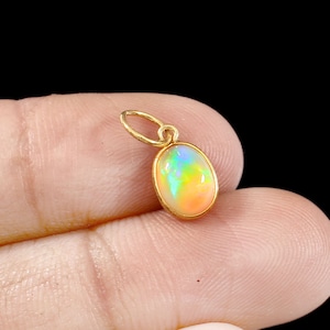 Pode incluir: Um pingente de ouro com uma gema de opala oval. A opala exibe um arco-íris de cores, incluindo rosa, laranja, amarelo, verde e azul.