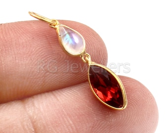 Puede incluir: Pendiente de oro con una piedra preciosa roja y una piedra de luna blanca. El pendiente está en una cadena de oro.