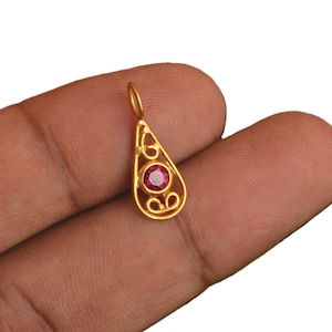 Könnte beinhalten: Ein goldener Anhänger in Tropfenform mit einem durchbrochenen Filigranmuster und einem einzelnen runden, facettierten rosa Edelstein in der Mitte. Der Anhänger verfügt über einen kleinen runden Ring an der Oberseite zur Befestigung an einer Kette.