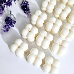 May include: A collection of white, round, decorative candles with a unique bubble design. Each candle has a single wick in the centre.
