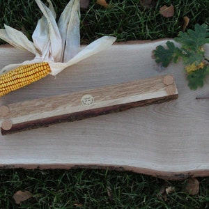 May include: A wooden serving tray with a natural wood finish and a live edge. The tray is made of two pieces of wood, one light and one dark, joined together. The tray has three wooden feet on the bottom. The tray is sitting on a green grassy surface.