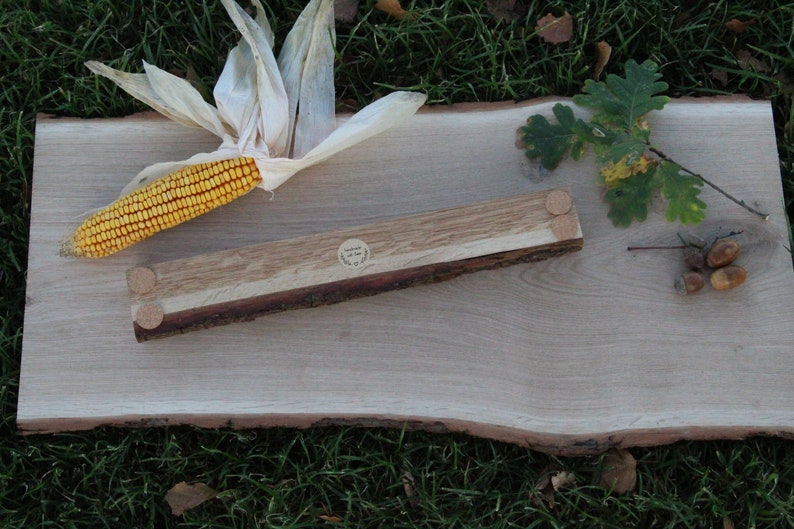 May include: A wooden serving tray with a natural wood finish and a live edge. The tray is made of two pieces of wood, one light and one dark, joined together. The tray has three wooden feet on the bottom. The tray is sitting on a green grassy surface.