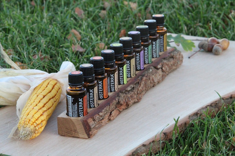 May include: A wooden log with a bark-like texture holds a row of ten small brown glass bottles with black caps. Each bottle has a white label with the word "dōTERRA" printed on it. The bottles are arranged in a line on the log, which is sitting on a light brown wooden surface.