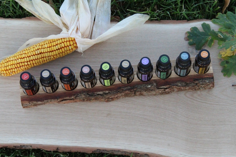 May include: A wooden essential oil holder with ten small glass bottles. The bottles are filled with colorful liquids and have black caps. The holder is on a wooden surface with a corn cob and husk in the background.