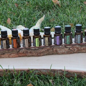 May include: A wooden stand with 12 small amber glass bottles with black caps. The bottles are labeled with the word "dōTERRA" and the name of an essential oil. The stand is sitting on a wooden surface.