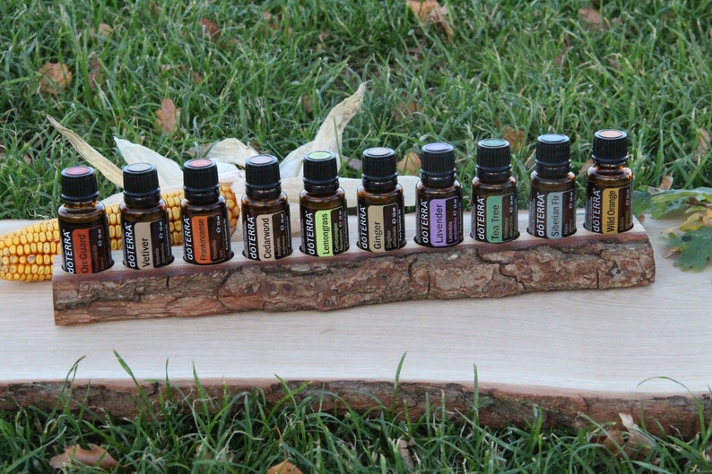 May include: A wooden stand with 12 small amber glass bottles with black caps. The bottles are labeled with the word "dōTERRA" and the name of an essential oil. The stand is sitting on a wooden surface.
