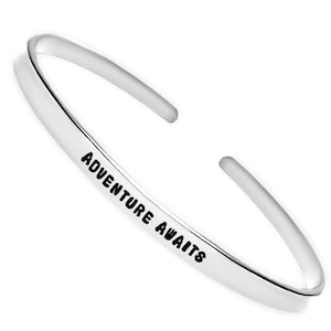 May include: A silver bangle bracelet with the words "Adventure Awaits" engraved on it.