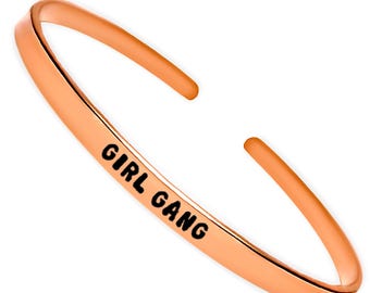 May include: A rose gold bangle bracelet with the words "GIRL GANG" engraved on it.