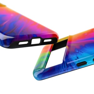 Może przedstawiać: Dwa kolorowe etui na telefon z wzorem tie-dye w odcieniach niebieskiego, r&oacute;żowego, ż&oacute;łtego i zielonego. Etui mają czarny gumowy zderzak wok&oacute;ł krawędzi.