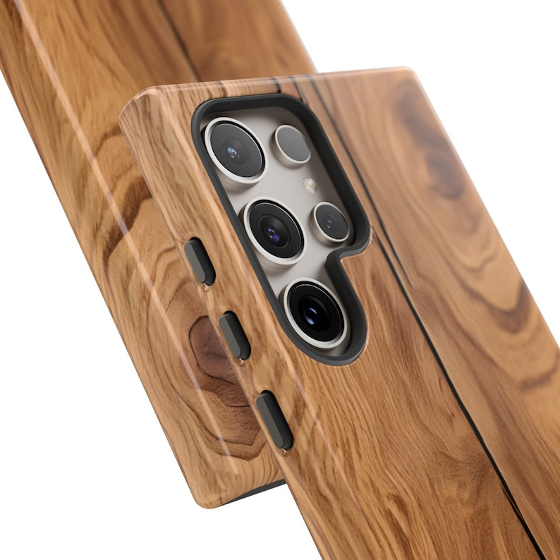 Może przedstawiać: Drewniana obudowa telefonu z brązowym wzorem słoj&oacute;w drewna. Obudowa ma wycięcie na obiektyw aparatu i przyciski.