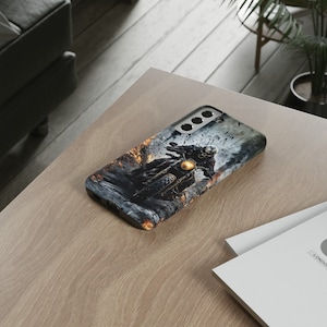 Puede incluir: Una funda de tel&eacute;fono negra con un gr&aacute;fico de una persona conduciendo una motocicleta a trav&eacute;s de un paisaje de fuego. La funda tiene un recorte para el objetivo de la c&aacute;mara.