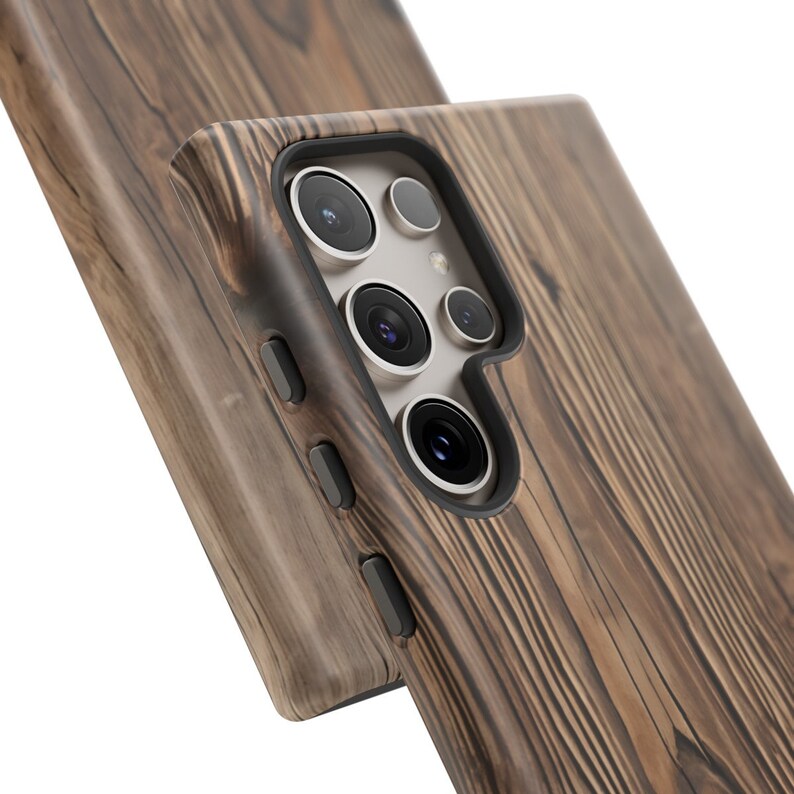 Op de afbeelding: Een bruine houten telefoonhoes met een zwarte camera-uitsparing en drie knoppen aan de zijkant. De hoes heeft een houtnerfpatroon.