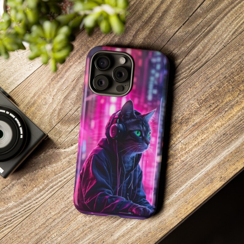 May include: A black cat wearing headphones and a hoodie, with a neon pink and blue city background. The cat is looking to the right. The image is on a phone case.