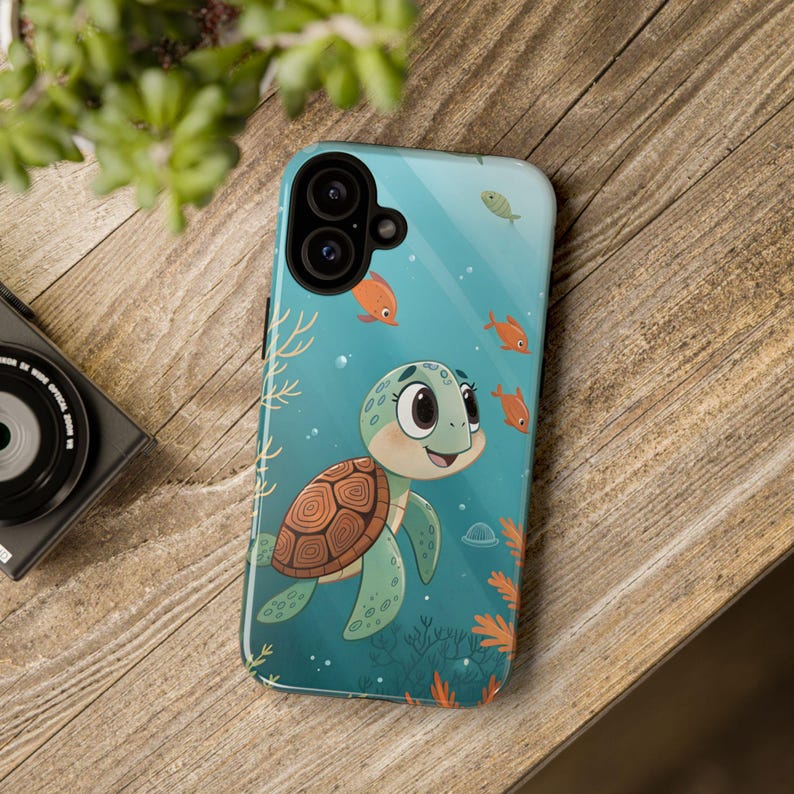 Może przedstawiać: Etui na telefon z kresk&oacute;wkowym ż&oacute;łwiem pływającym pod wodą z pomarańczowymi rybami. Etui ma turkusowe tło z koralowcami i bąbelkami. Ż&oacute;łw ma zielone ciało i brązowy pancerz.