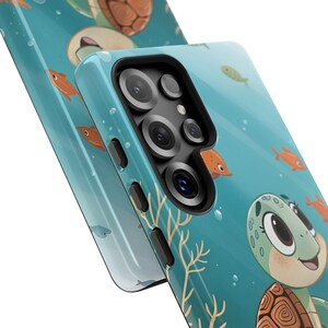 Może przedstawiać: Turkusowe etui na telefon z kresk&oacute;wkowym wzorem ż&oacute;łwia, pomarańczowymi rybami i koralowcami na niebieskim tle. Etui ma błyszczące wykończenie i wycięcie na aparat. Projekt zawiera bąbelki i przyjaznego ż&oacute;łwia.
